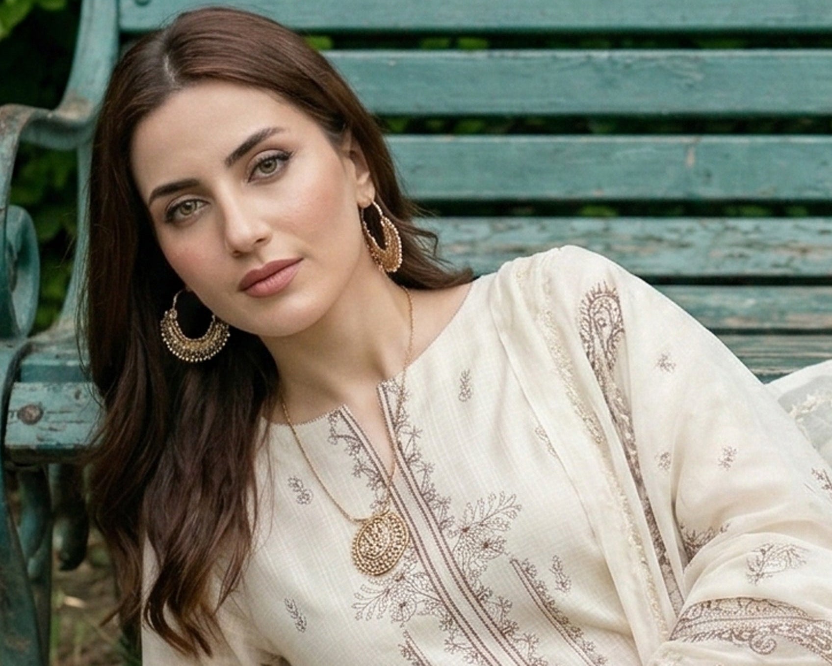Woman in a cream embroidered outfit sitting on a wooden bench outdoors.